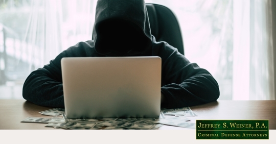 faceless person in hoodie on laptop surrounded by money