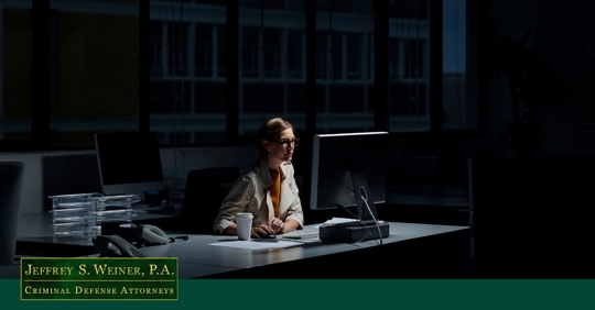 woman sitting at desk in dimly lit room, looking at computer screen