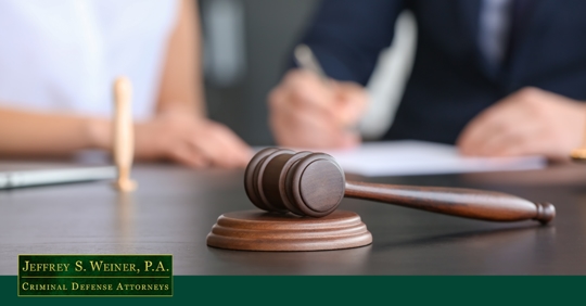 gavel in focus with a blurred background showing an attorney and client having a discussion with a paper in front of them